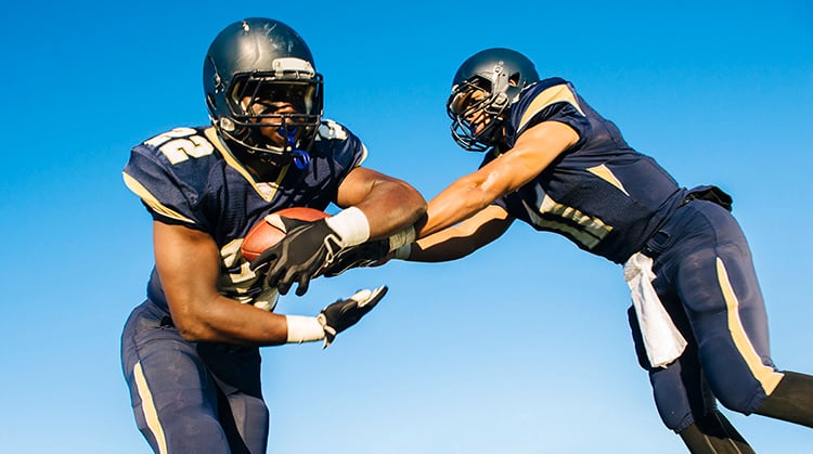 A quarterback hands off a football to a teammate.